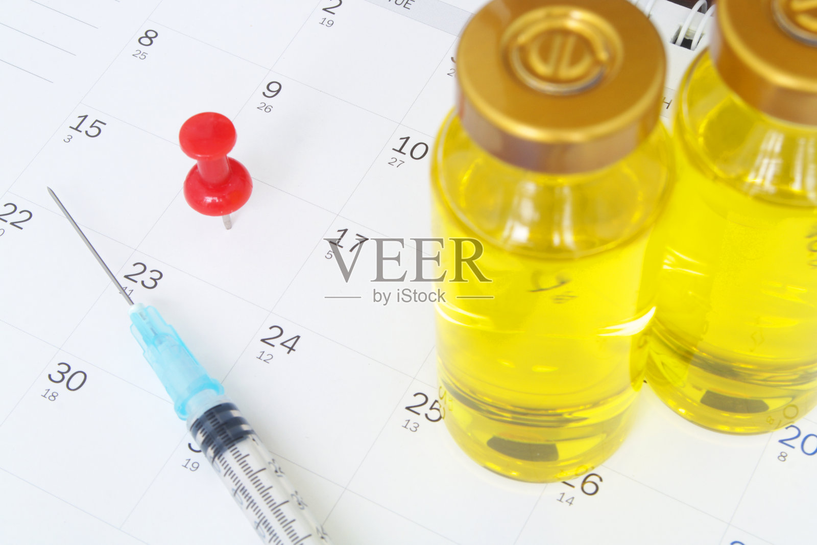 日历上的疫苗瓶、图钉和注射器。照片摄影图片