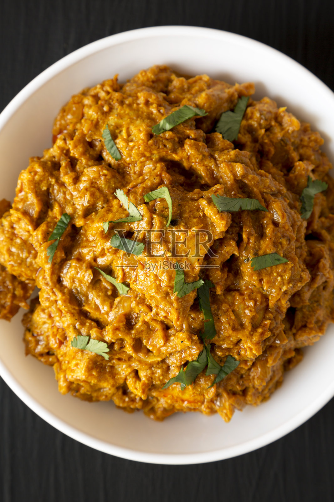 自制的咖喱鸡放在白色的碗里，在黑色的表面上，俯视图。平躺着，从上面俯视。照片摄影图片