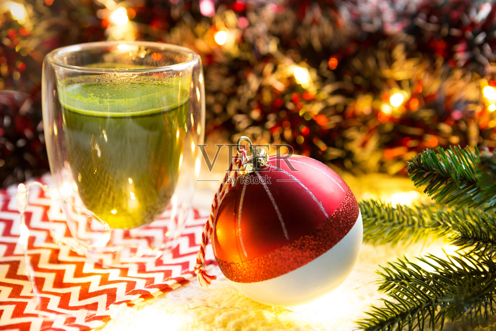 透明双层玻璃玻璃杯，桌上放着日本抹茶，圣诞装饰。新年的气氛，花环和金属丝，云杉枝，舒适，针织毯子，球，条纹餐巾照片摄影图片