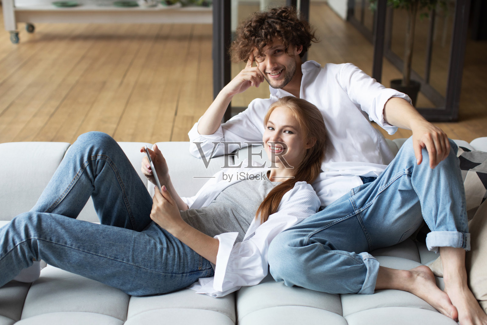 男人和女人在客厅的沙发上休息，用着数字平板电脑。照片摄影图片