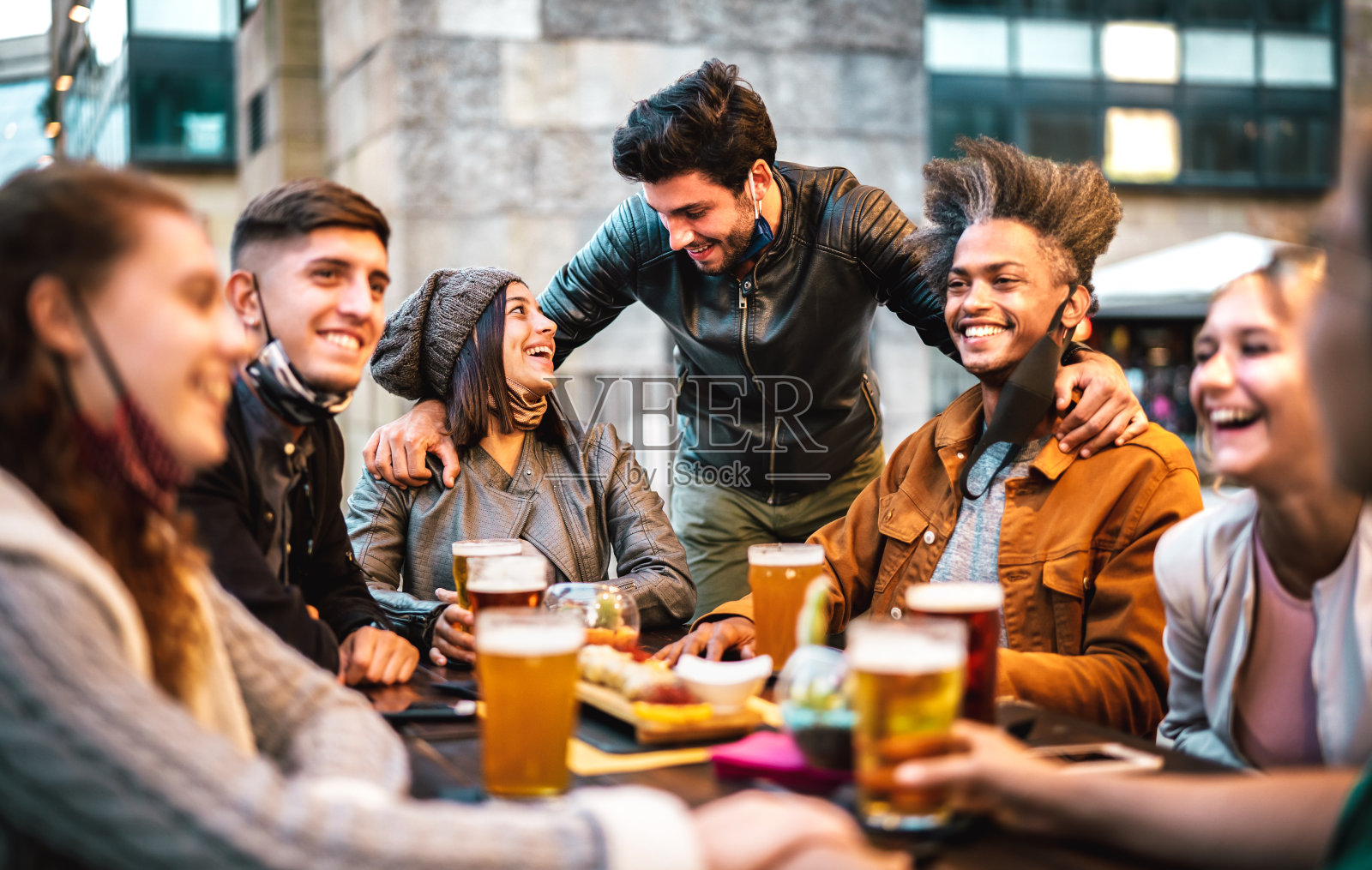 年轻人带着面罩喝啤酒-新常态的生活理念与千禧一代在啤酒厂酒吧外的欢乐时光一起聊天-以中心人物为焦点的暖滤照片摄影图片