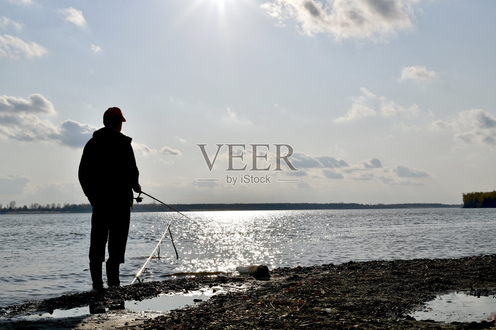 一个渔夫的剪影，手拿纺锤，鱼在河上，映衬着蓝色的水和天空。照片摄影图片