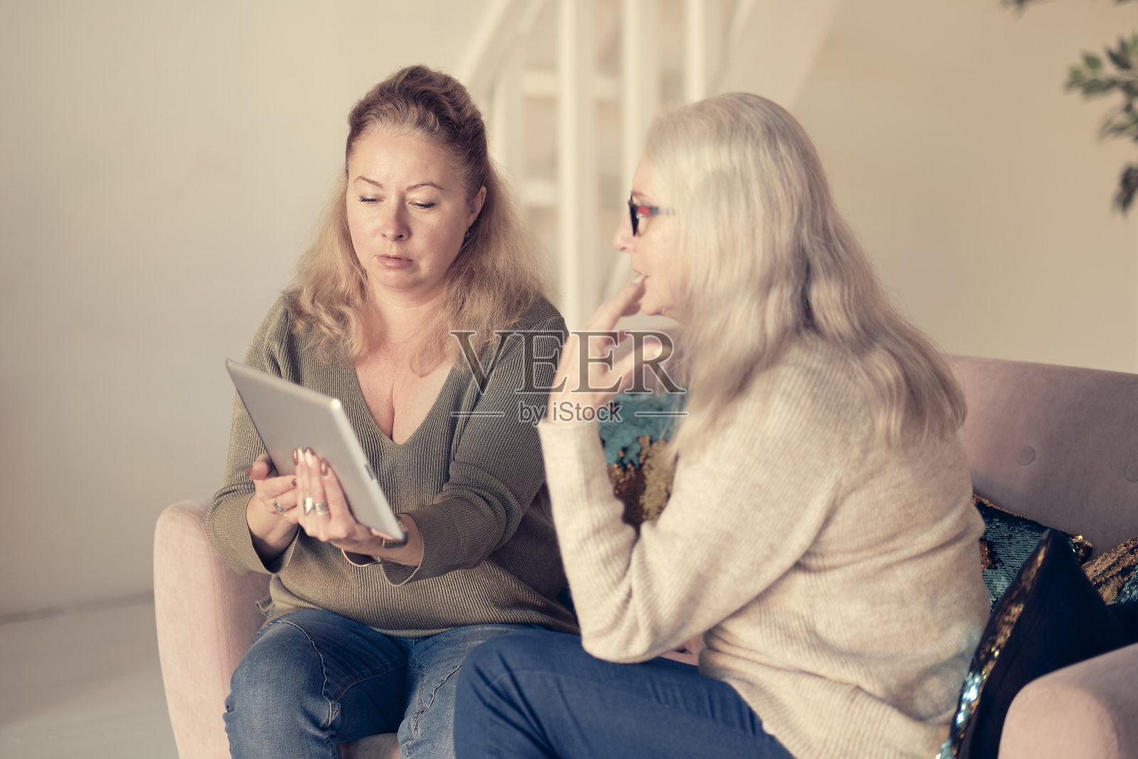 教年长母亲在家使用互联网的妇女。妇女和她的女儿在室内看现代小玩意。一起放松，不同年代的爱好消遣。对长者的支援照片摄影图片