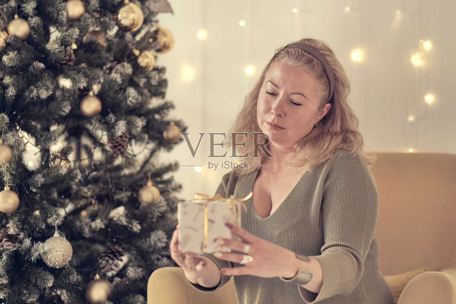 悲伤的女人在圣诞树旁沉思。悲伤孤独的女人在圣诞节坐在家里客厅的沙发上抱怨。柔和的焦点，暖色调照片摄影图片