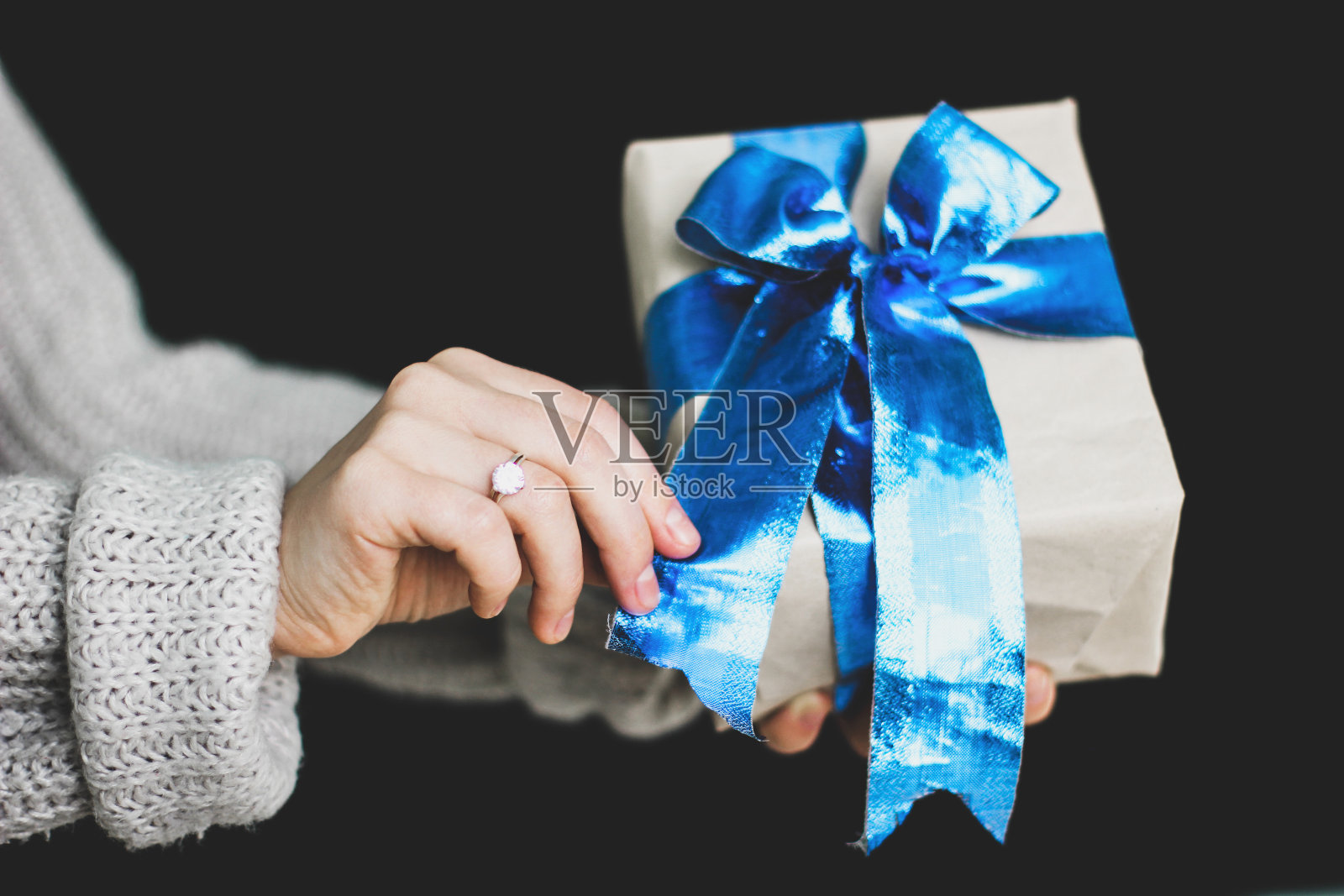 这个女孩手里拿着一份礼物，上面有一个蓝色的蝴蝶结。用牛皮纸做的礼物。美丽的蓝色蝴蝶结。一个圣诞礼物。新年。惊喜照片摄影图片