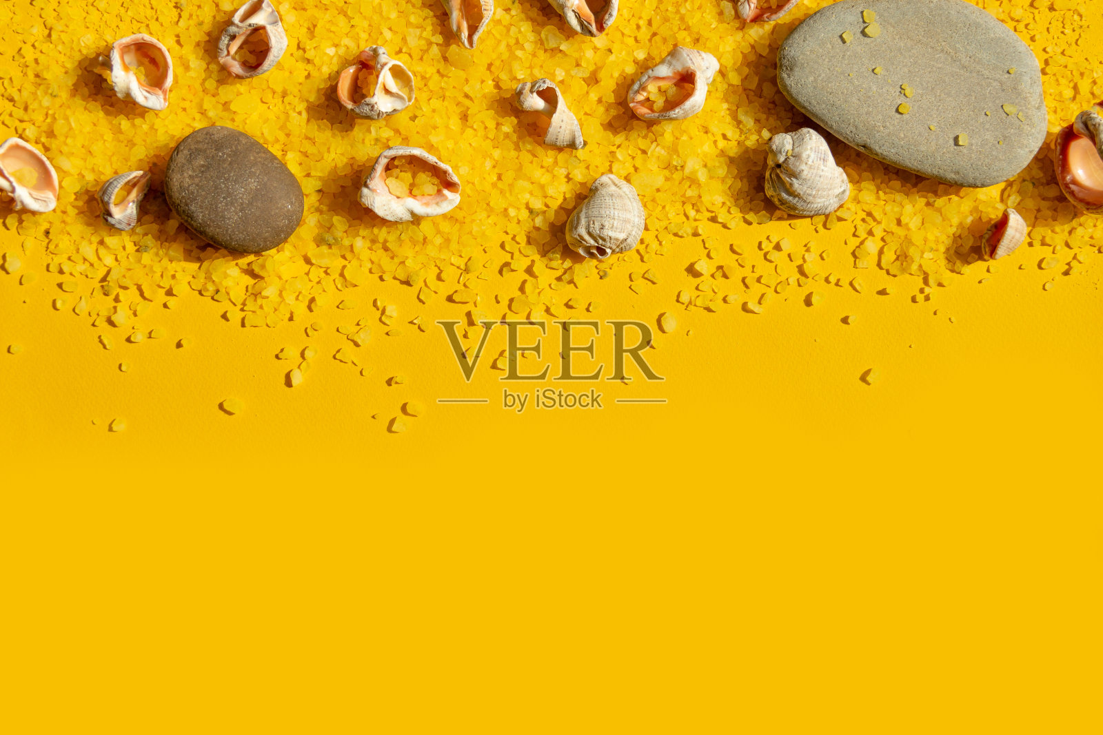 贝壳和石头在明亮的黄色沙子背景。夏季背景与明亮的阳光。旅游度假概念照片摄影图片