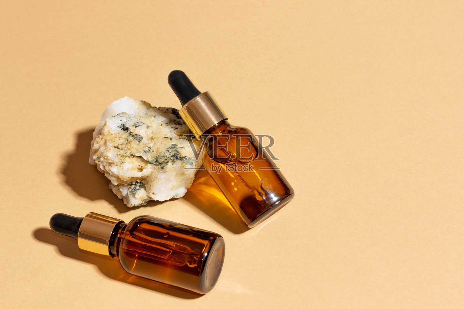 在明亮的阳光下，米色背景的石头旁边有一个滴管，玻璃瓶里的天然化妆品。天然化妆品的概念，天然精油照片摄影图片