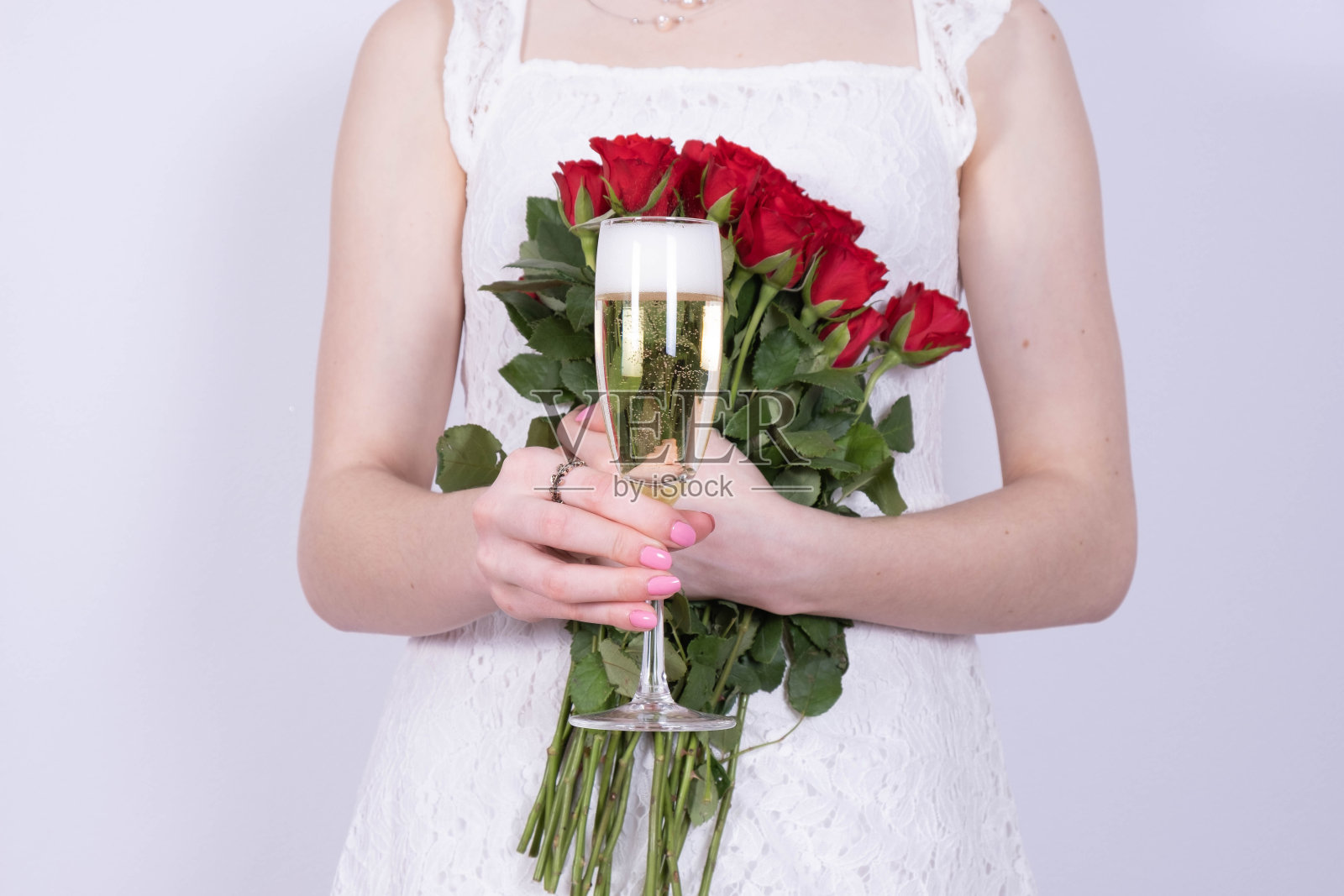 一个穿着白色连衣裙的女孩手里拿着一束玫瑰，另一个手里拿着白色背景上的一杯香槟照片摄影图片