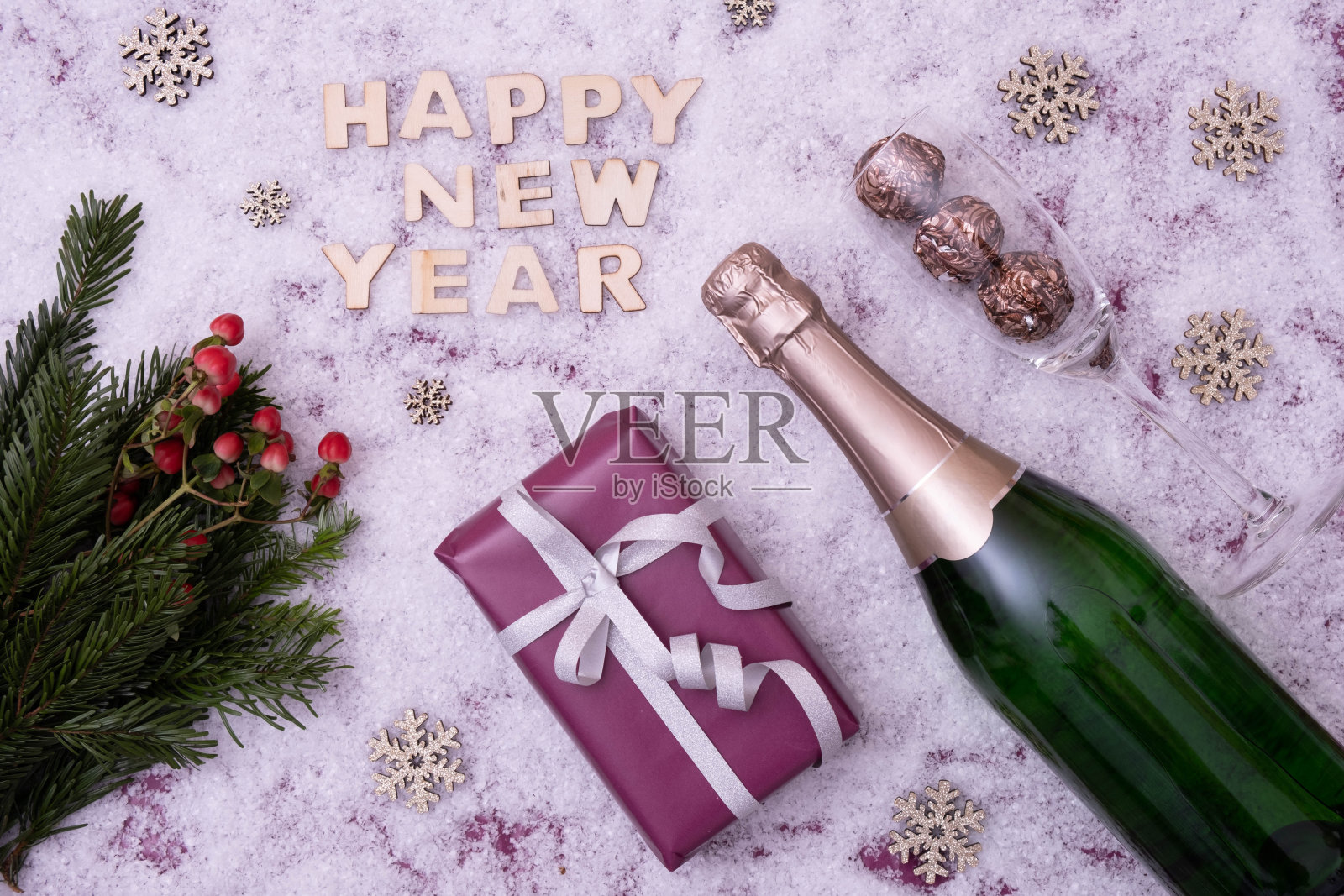 新年的礼物，云杉树枝，一瓶香槟，红浆果躺在喜庆的桌子旁，旁边写着:“新年快乐”的雪景照片摄影图片