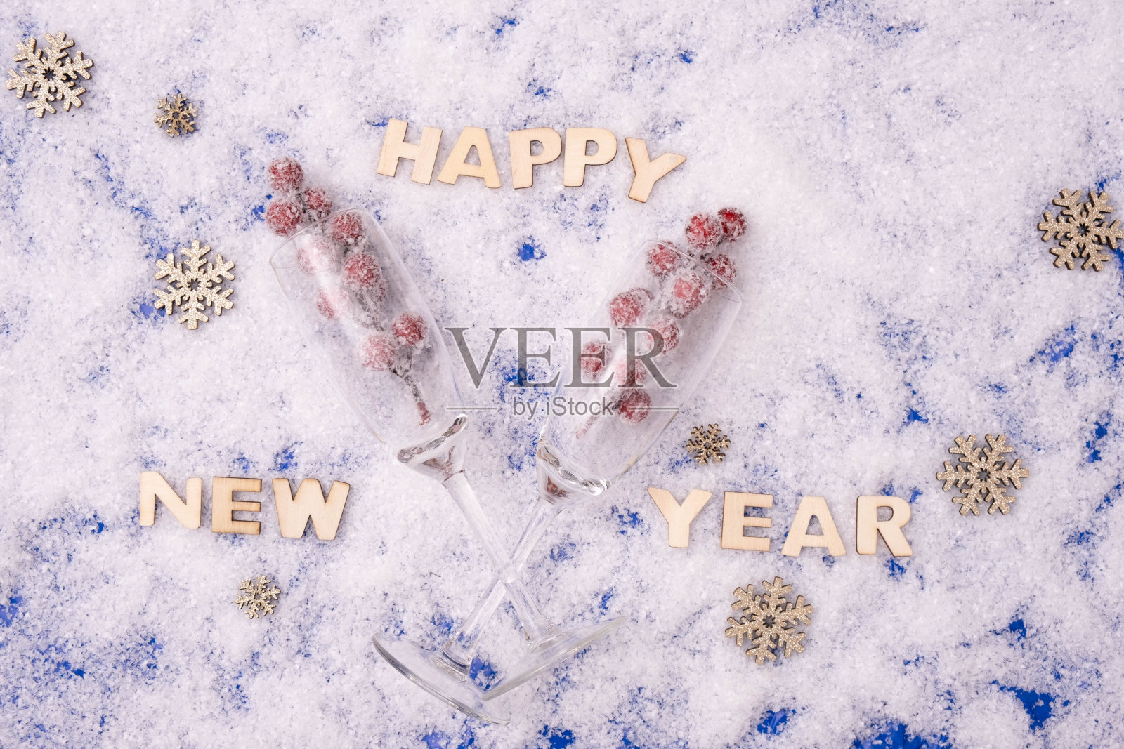 节日的桌子上放着香槟酒杯和一份礼物，旁边写着:“新年快乐”，背景是雪景照片摄影图片