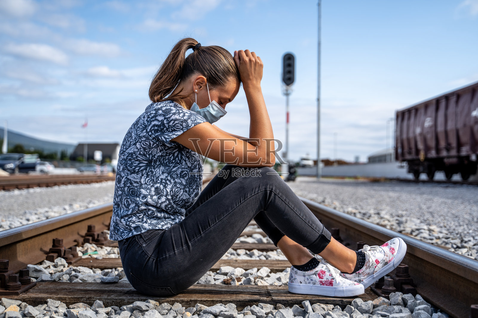 悲伤的年轻女子坐在铁轨上戴着防护面罩照片摄影图片