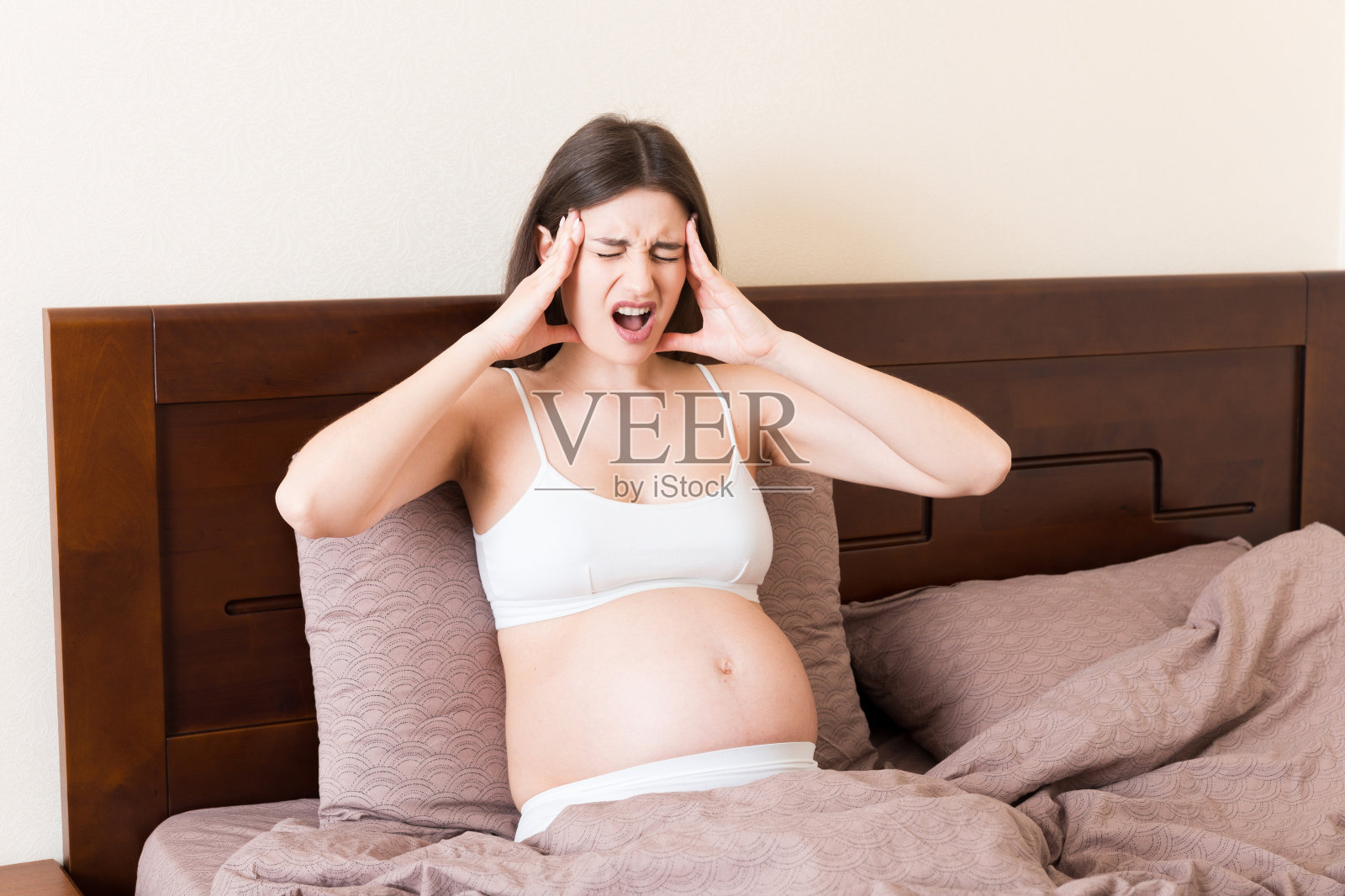 年轻漂亮的孕妇在床上饱受头痛之苦照片摄影图片