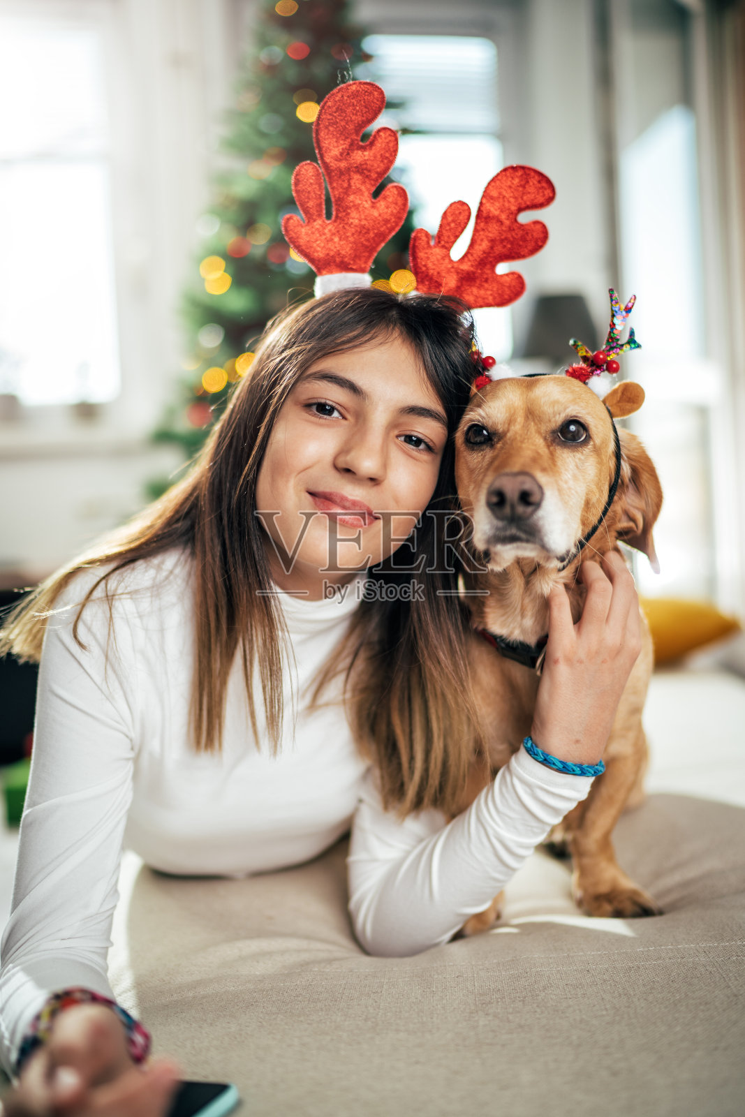 一个女孩和一只长着鹿角的狗在圣诞树旁摆姿势照片摄影图片