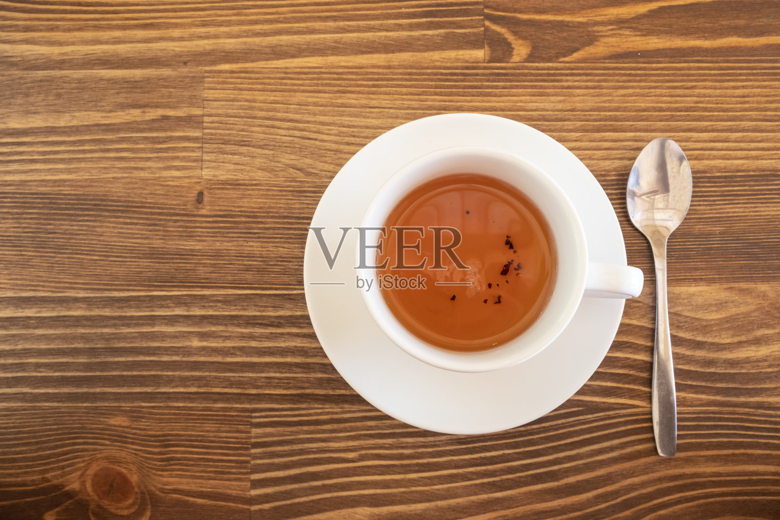 棕色的木桌背景上放着一杯白色的茶和一茶匙。照片摄影图片