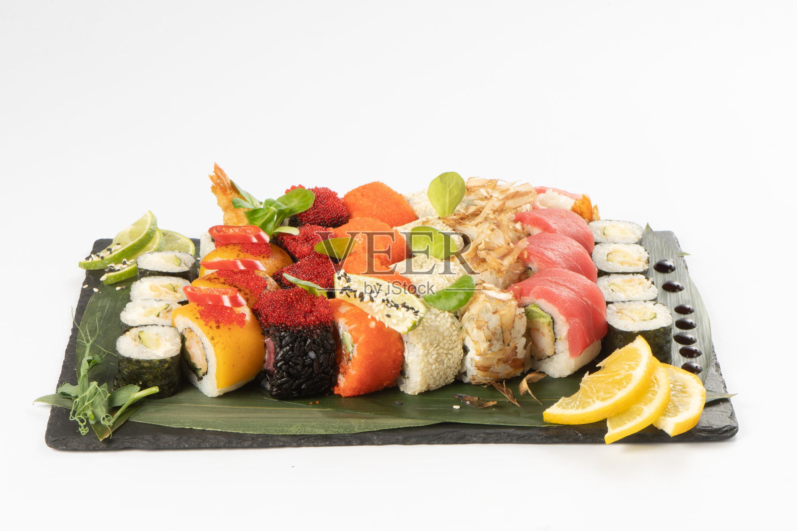 各种各样的寿司，由鲑鱼，金枪鱼，虾卵tobiko飞鱼，米饭和芝麻在一个黑色的石板石平台上，点缀竹叶，照烧酱。照片摄影图片