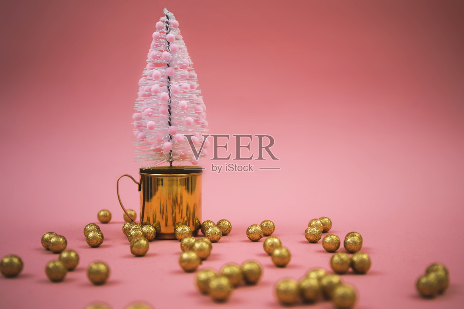 粉红色装饰的圣诞树和粉红色背景上的金色装饰球。照片摄影图片