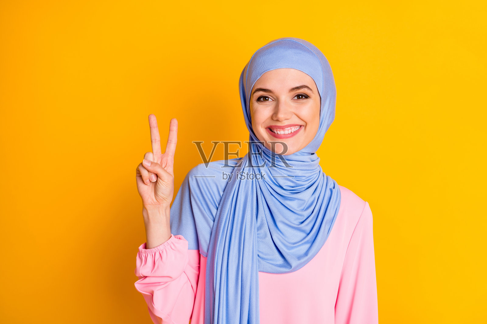特写的漂亮迷人的愉快的穆斯林女士显示v-sign孤立在明亮的黄色背景照片摄影图片