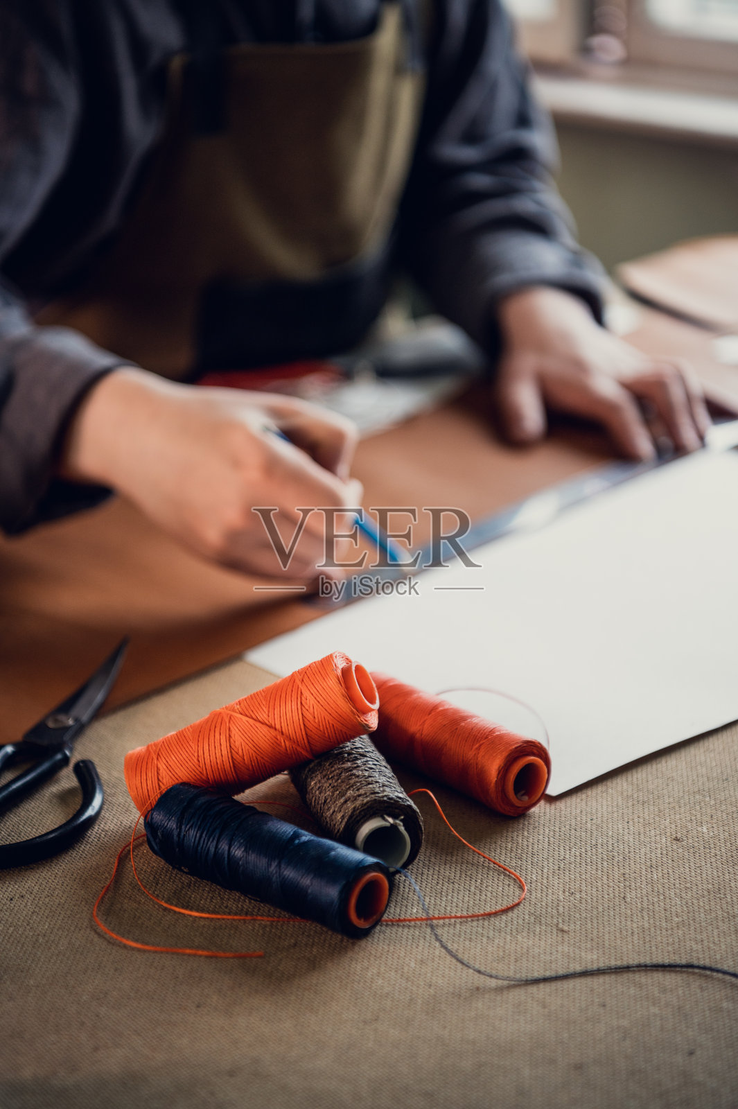 近景照片与景深的线线圈在前景。一个鞋匠在一个有窗户的车间的桌子上工作照片摄影图片