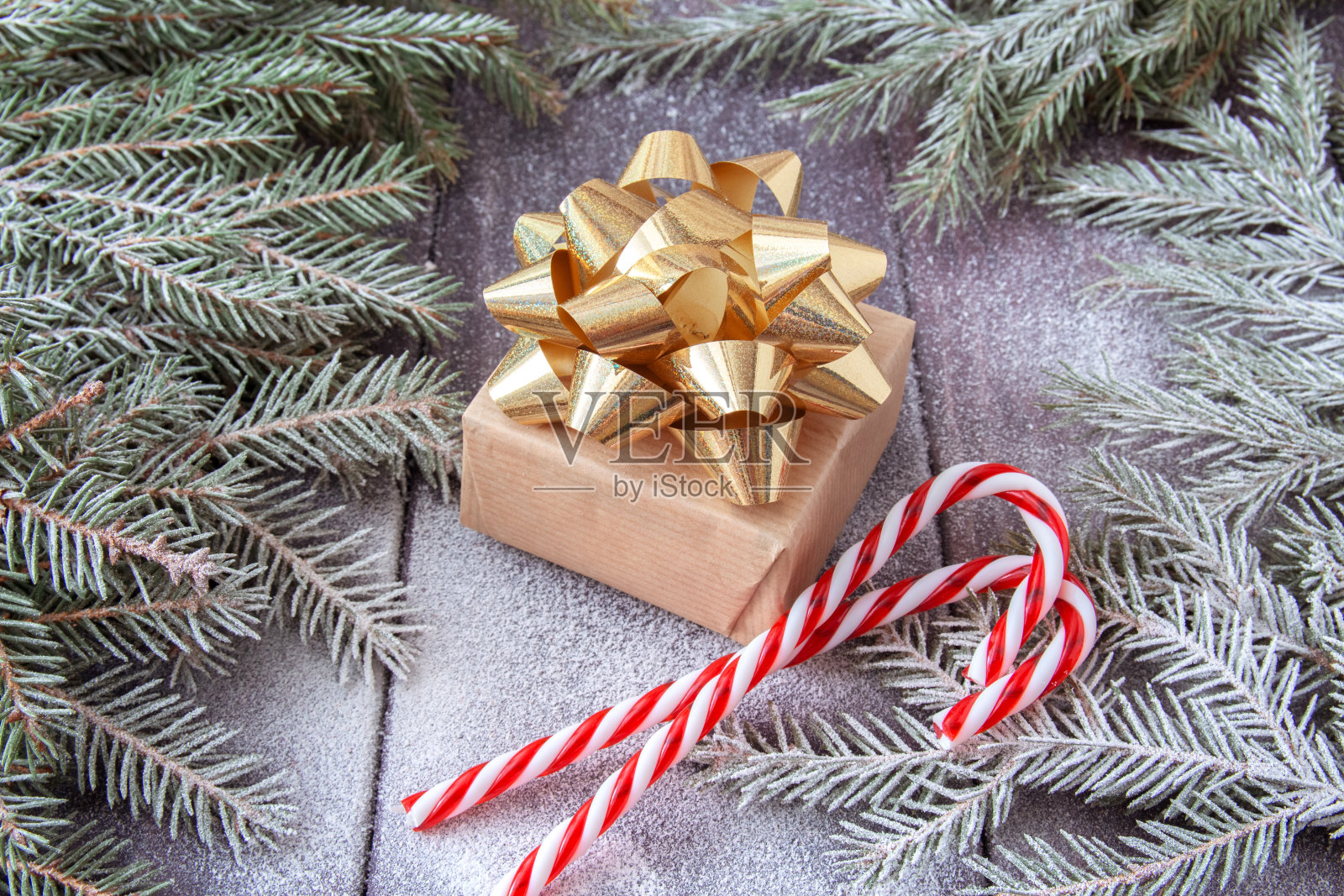 圣诞礼盒包装在牛皮纸与金色丝带和红色圣诞糖果在雪覆盖的深色木制背景与冷杉枝照片摄影图片