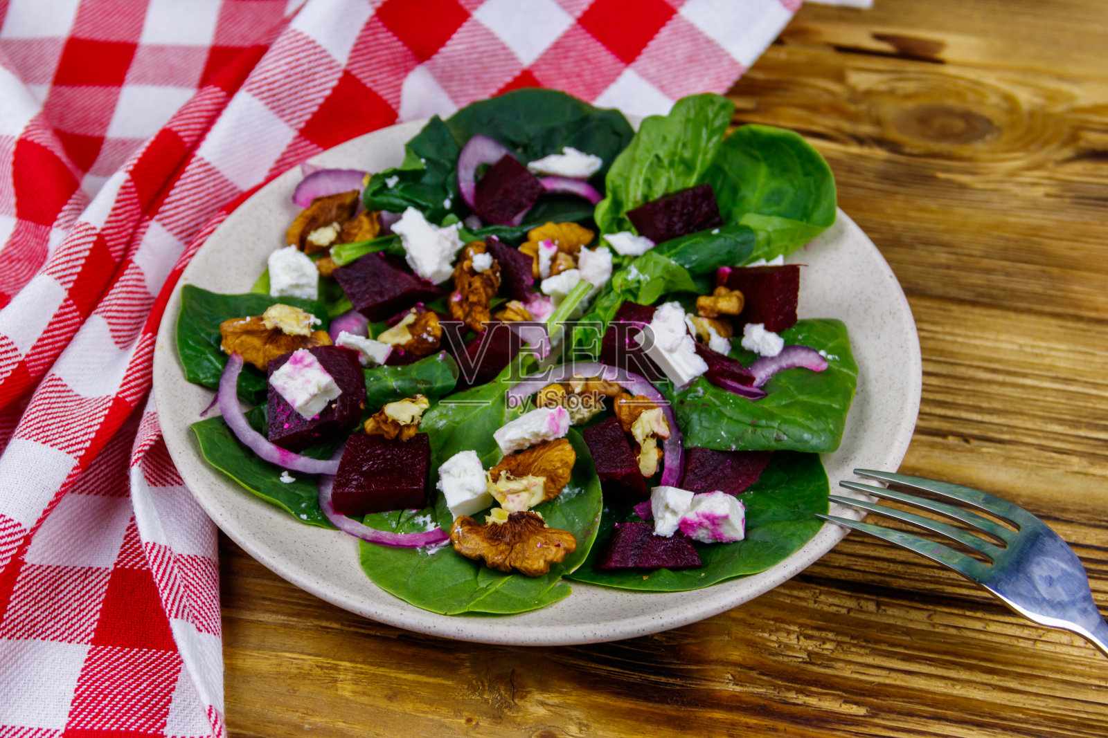 美味的菠菜沙拉配煮甜菜根，羊乳酪，核桃和红洋葱在木桌上。健康的素食照片摄影图片