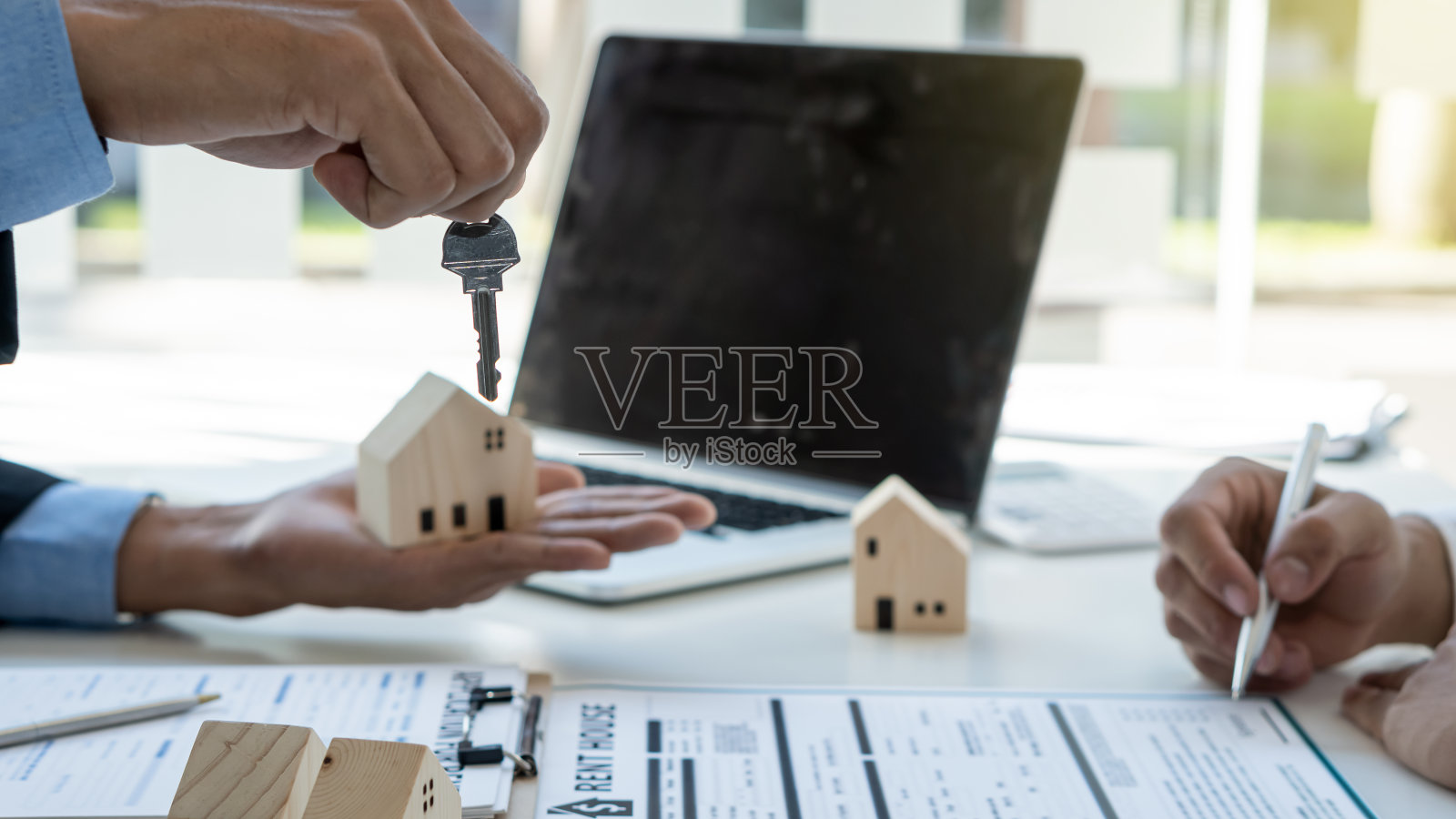 房地产经纪人会在客户的办公桌上放着家用模型和笔记本电脑，在办公室里签订合同后，为客户保管钥匙和房子。照片摄影图片