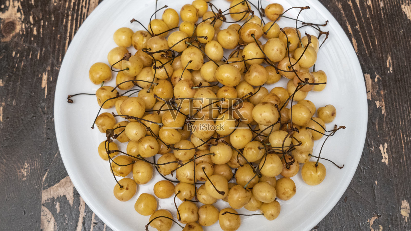 一串成熟的甜的黄樱桃。白色盘子上新鲜的黄色樱桃俯视图。新鲜的夏季背景。有机的概念。照片摄影图片