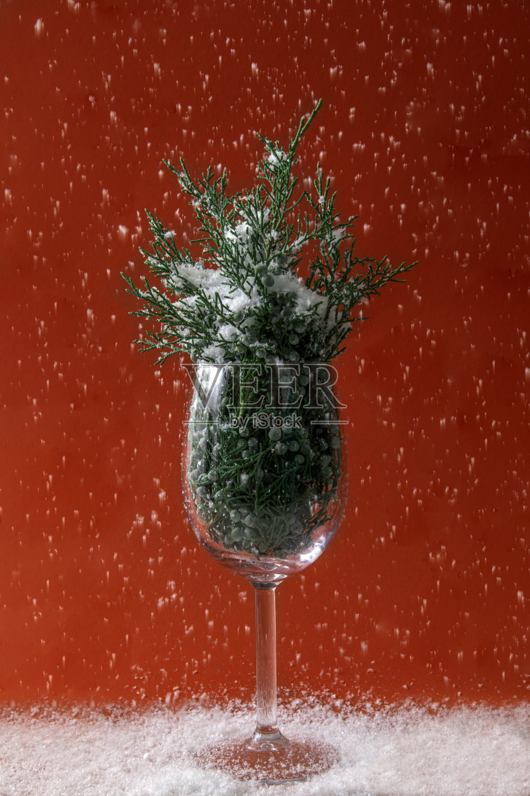 酒杯里装满了圣诞树，白雪点缀着红色的背景，假期开始了照片摄影图片