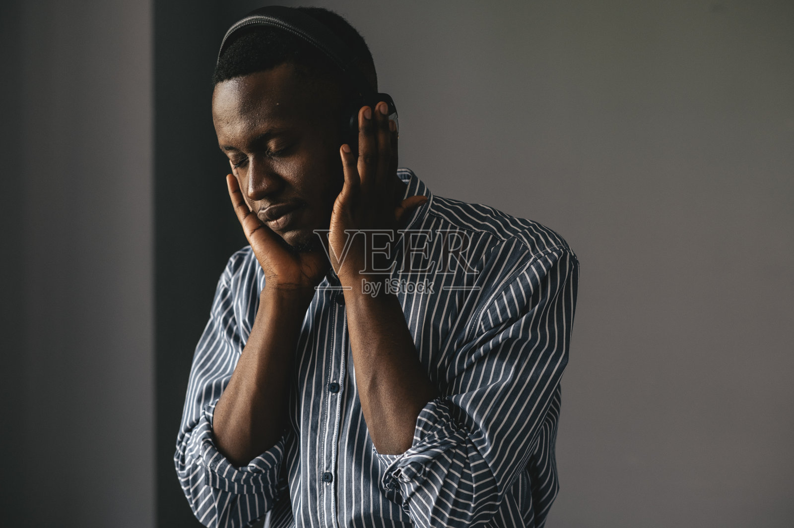 一个黑皮肤的家伙在灰色的背景下听着音乐，享受着美丽的抒情音乐照片摄影图片