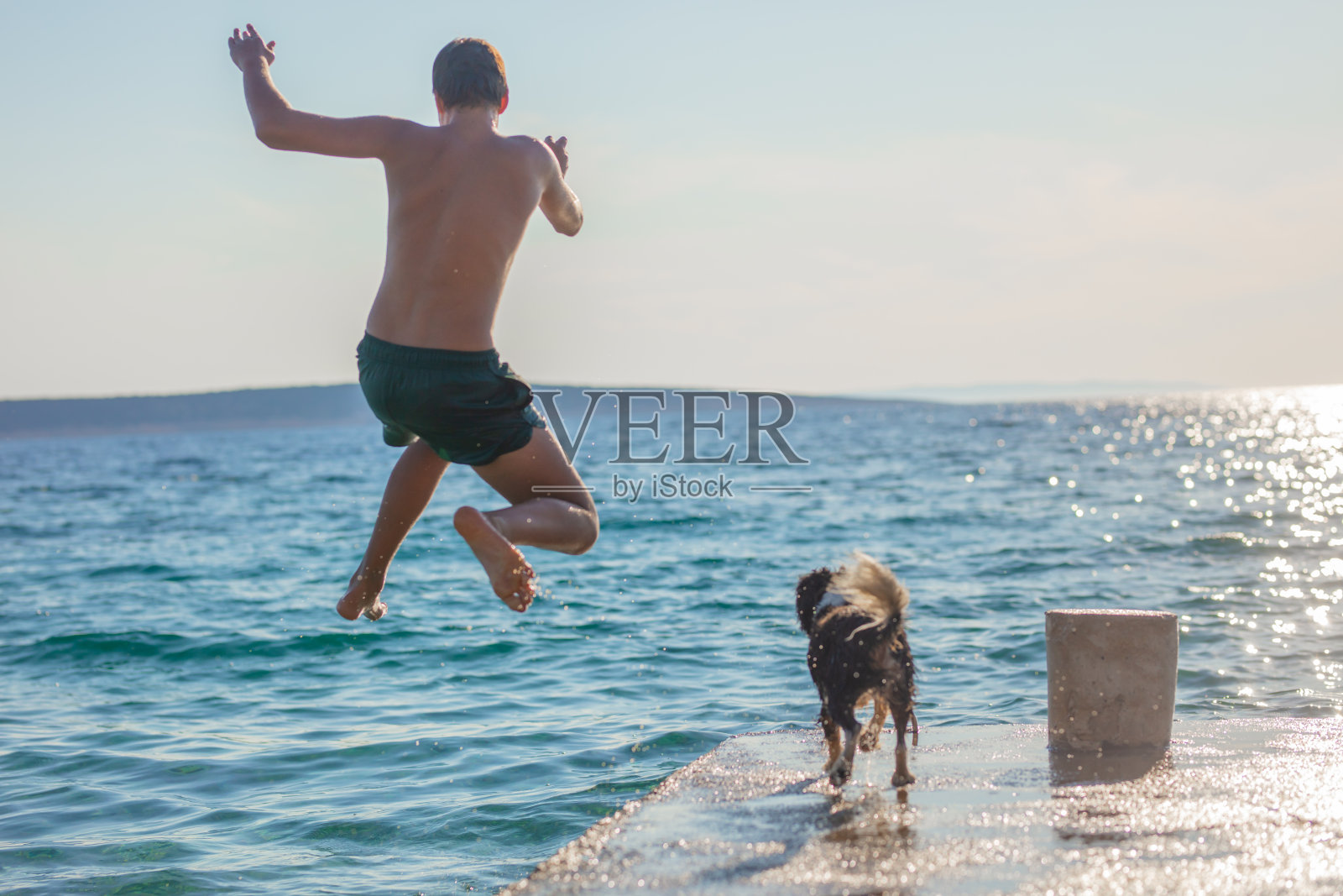 男孩跳进水里，狗在海边照片摄影图片