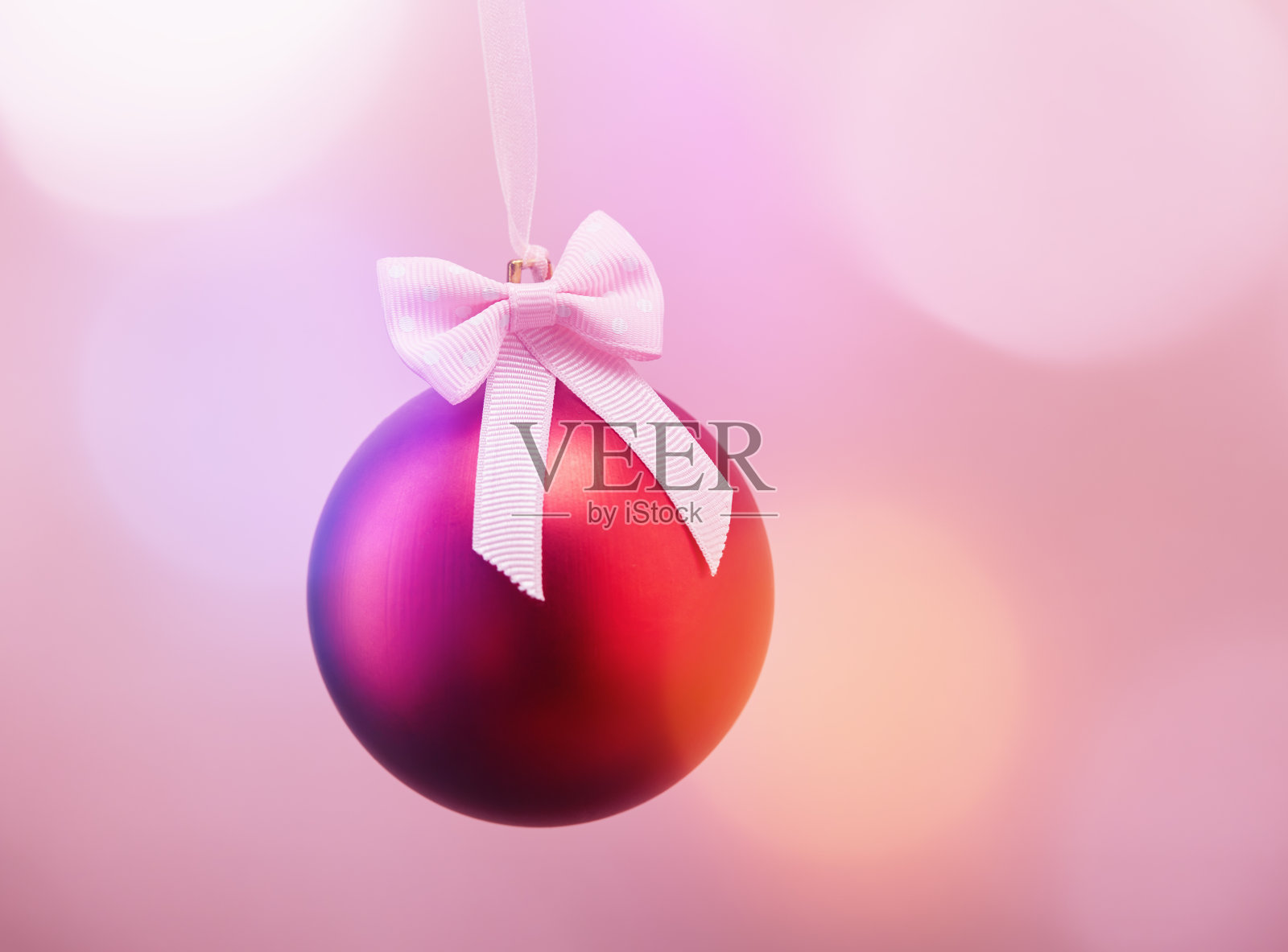 红色的圣诞球挂在带蝴蝶结的缎带上，背景是柔软的散焦球照片摄影图片