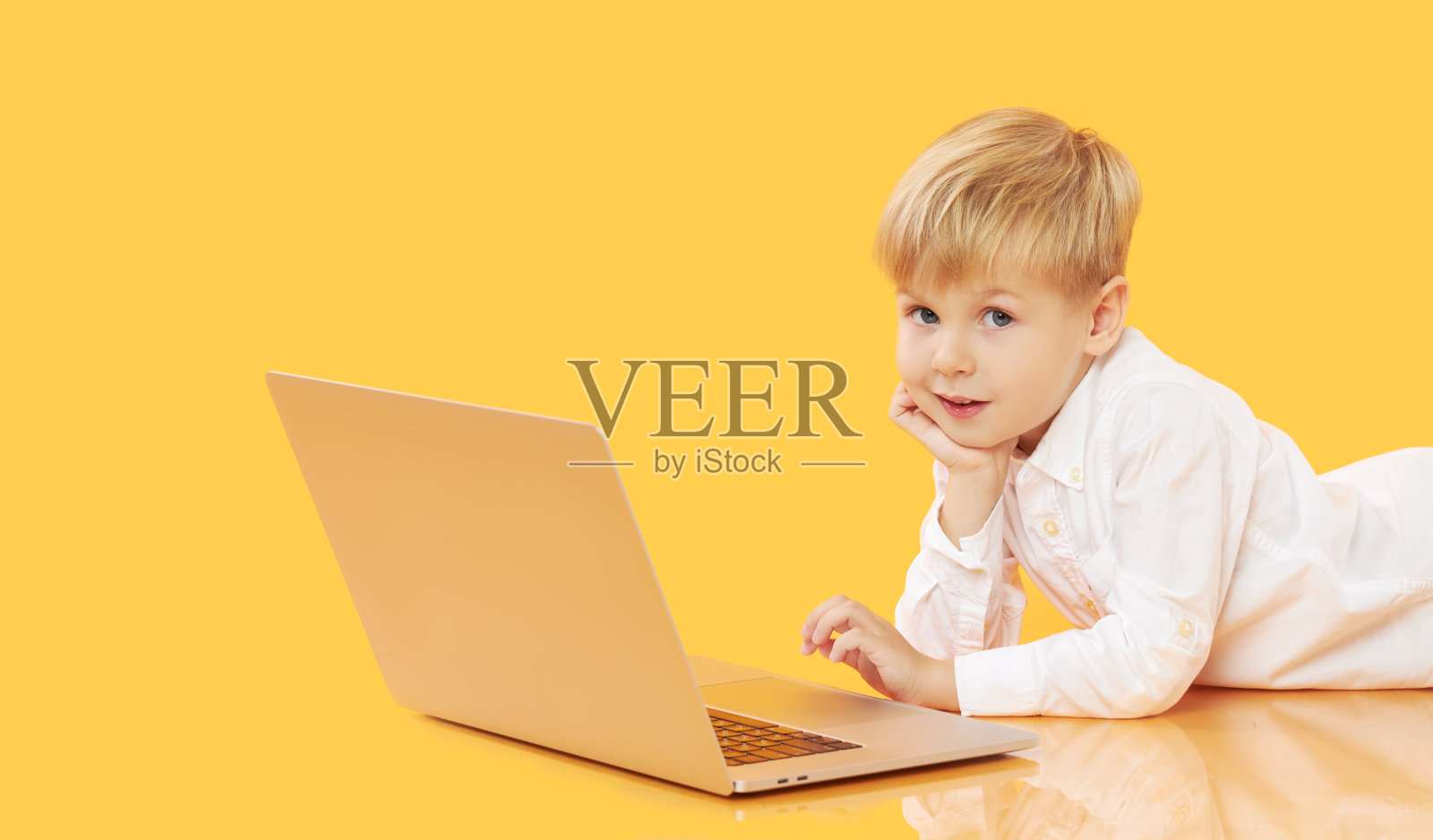 一个小男孩用黄色背景的笔记本电脑。教育，在线学习，在家学习，远程学习。隔离期间的小学生照片摄影图片