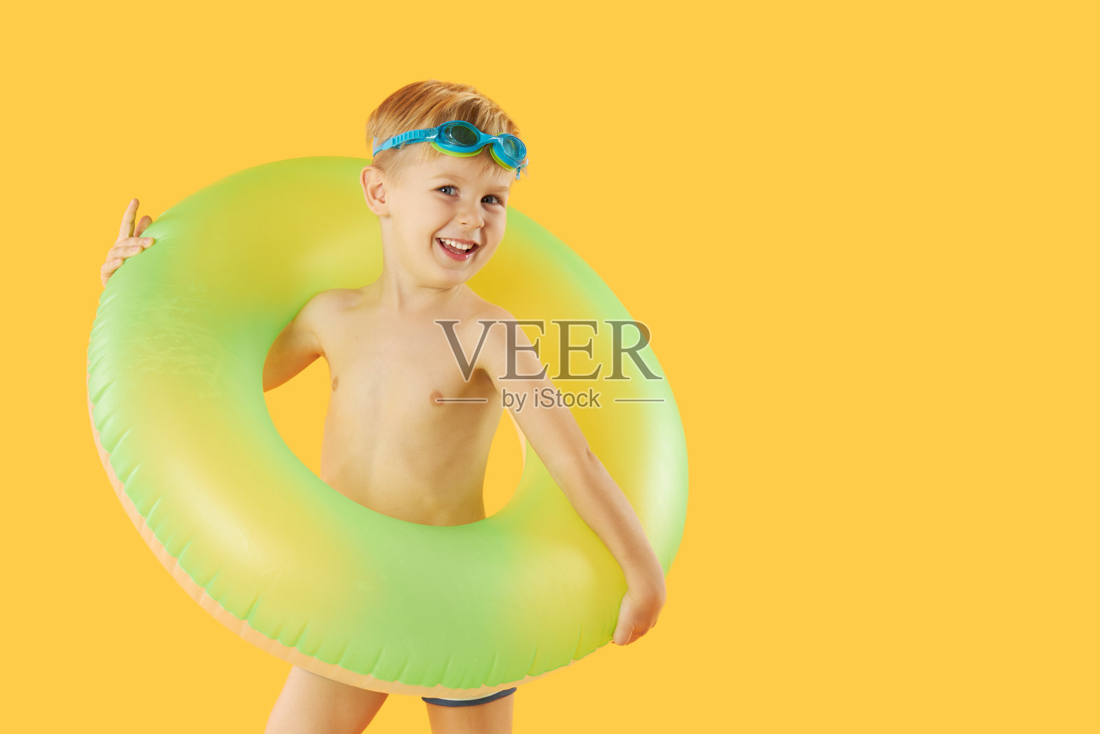 微笑的快乐的孩子男孩的肖像游泳镜与霓虹灯充气橡胶圈有乐趣孤立在黄色背景。暑假6滑稽的脸照片摄影图片