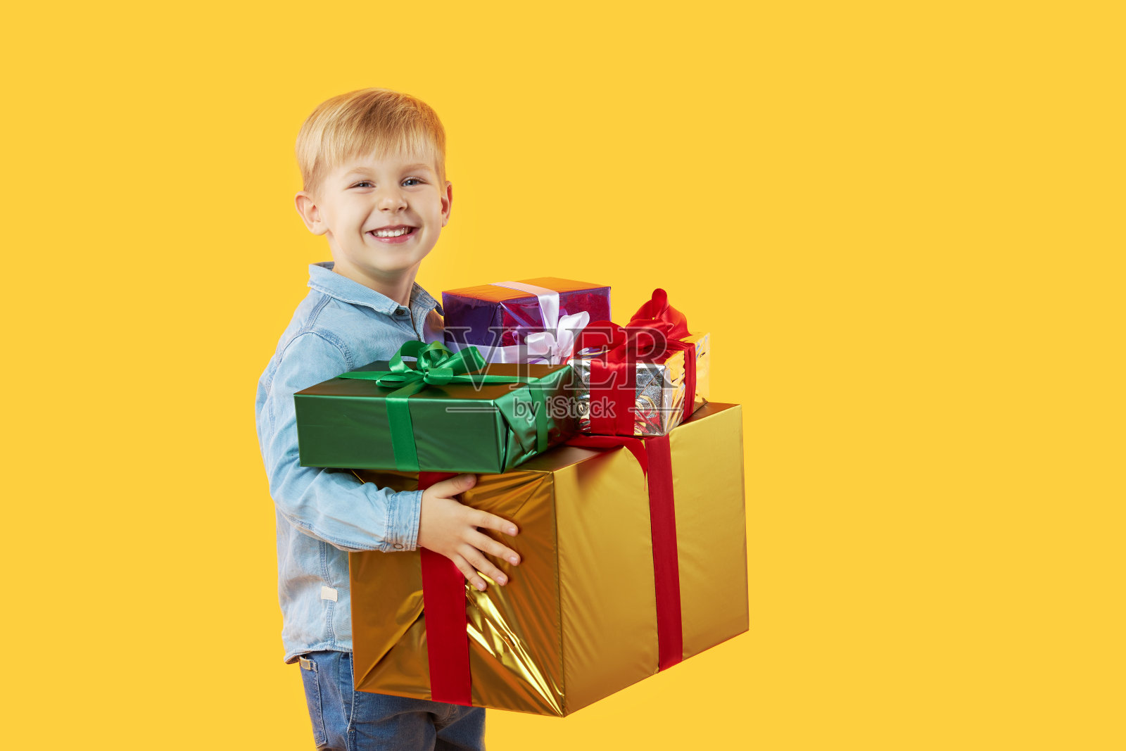 快乐可爱的孩子男孩的肖像拿着礼盒，看着孤立的黄色背景相机。有趣的脸照片摄影图片