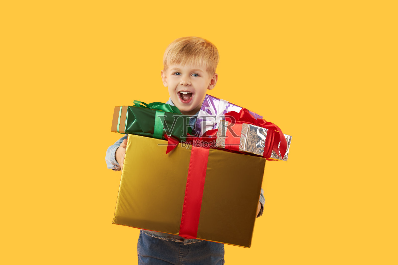 快乐可爱的孩子男孩的肖像拿着礼品盒，看着相机孤立在黄色背景照片摄影图片