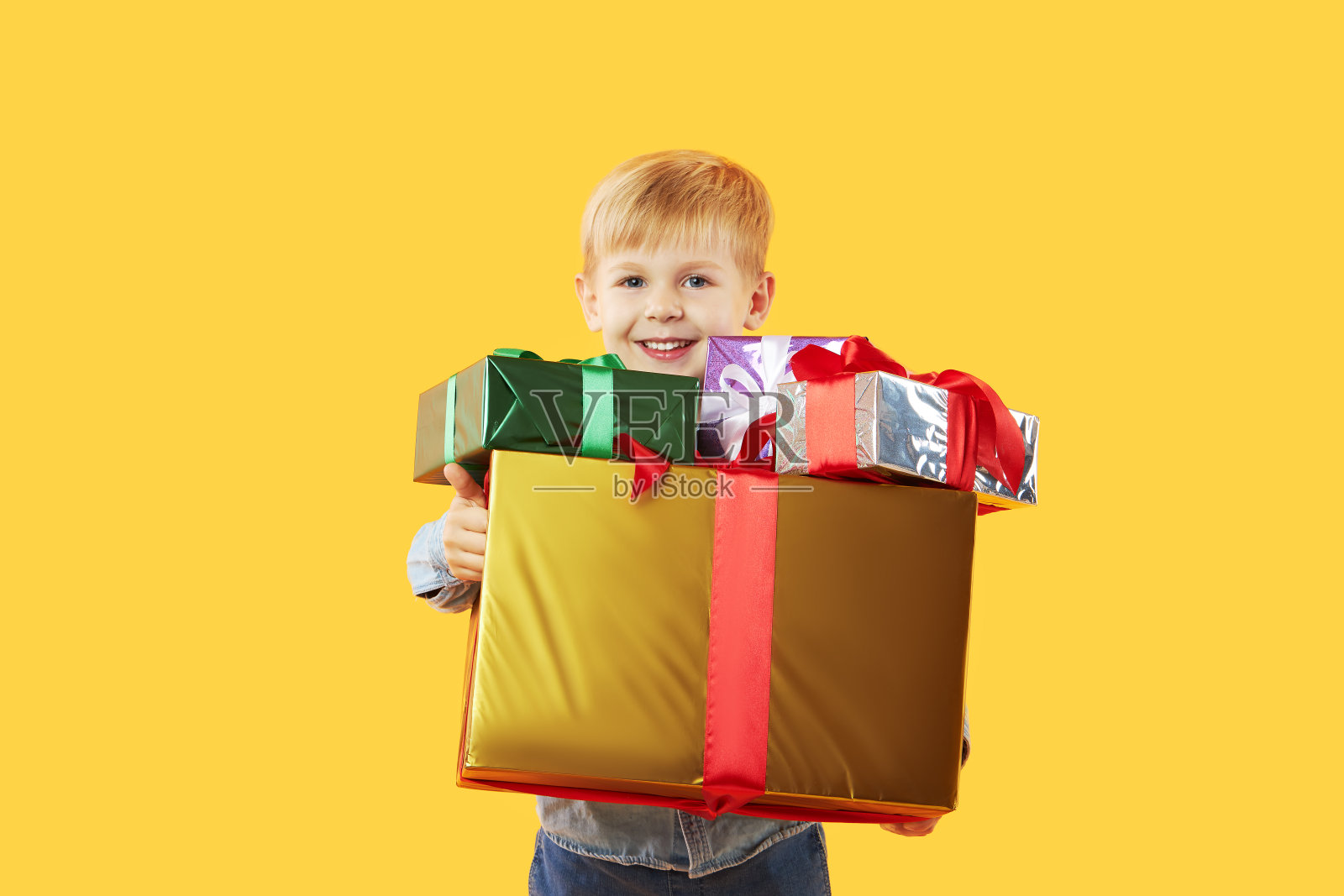 快乐可爱的孩子男孩的肖像拿着礼盒，看着孤立的黄色背景相机。有趣的脸照片摄影图片