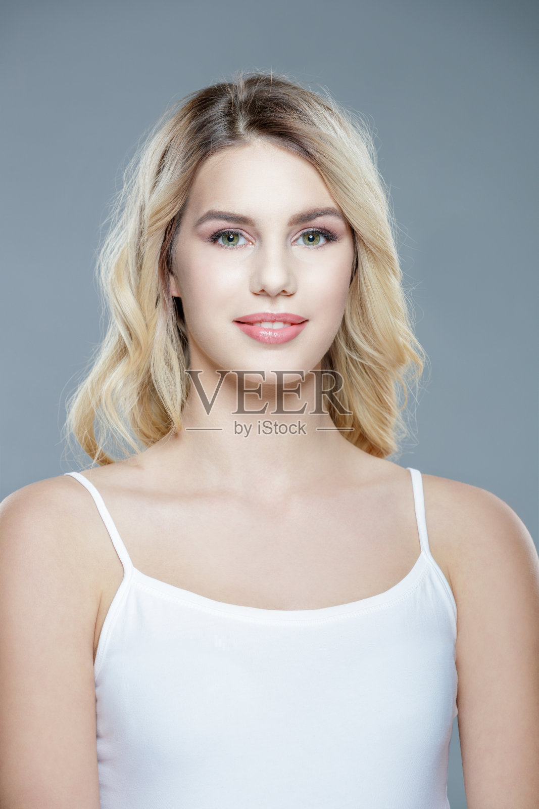 漂亮的金发年轻女子，穿着背心，披头散发，对着镜头微笑照片摄影图片