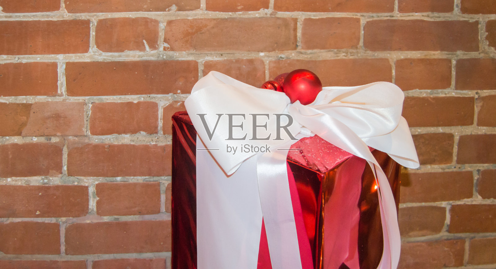 红色砖墙背景上有一个白色蝴蝶结的圣诞礼盒。查看与空间的副本照片摄影图片