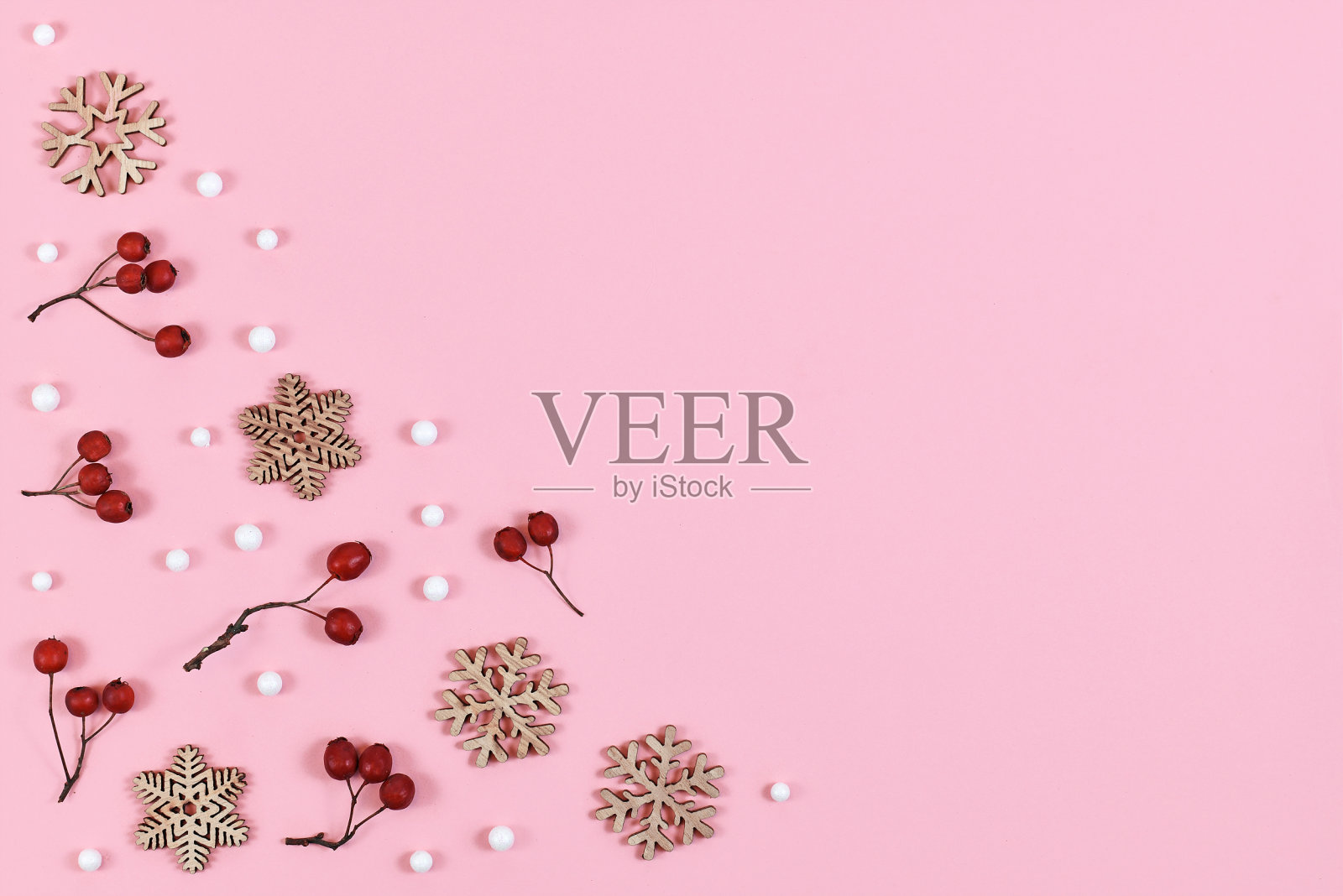 红色的浆果、白色的雪球和木制的雪花装饰在浅粉色背景的角落里照片摄影图片