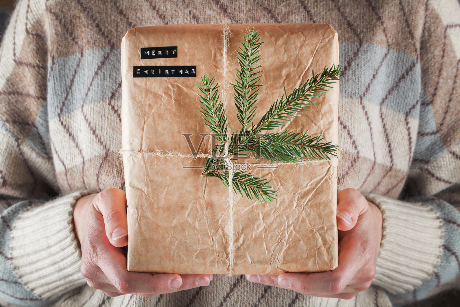不认识的女孩在米色和蓝色毛衣拿着环保礼盒的工艺包装纸与树枝。圣诞节，新年现在的概念。照片摄影图片
