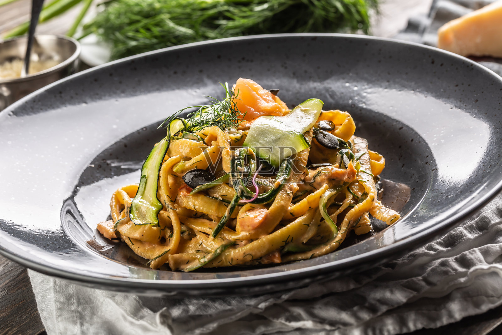 熏鲑鱼，西葫芦，南瓜子和新鲜茴香的意大利扁面放在一个深色的盘子里。照片摄影图片