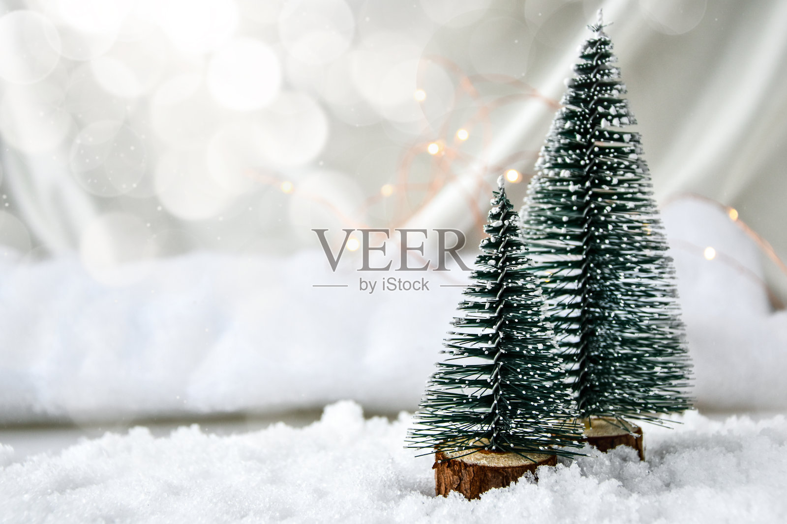 两棵圣诞树在香槟色的丝绸背景和白色的雪。时髦的装饰。圣诞节的庆祝活动。新年的概念。贺卡照片摄影图片