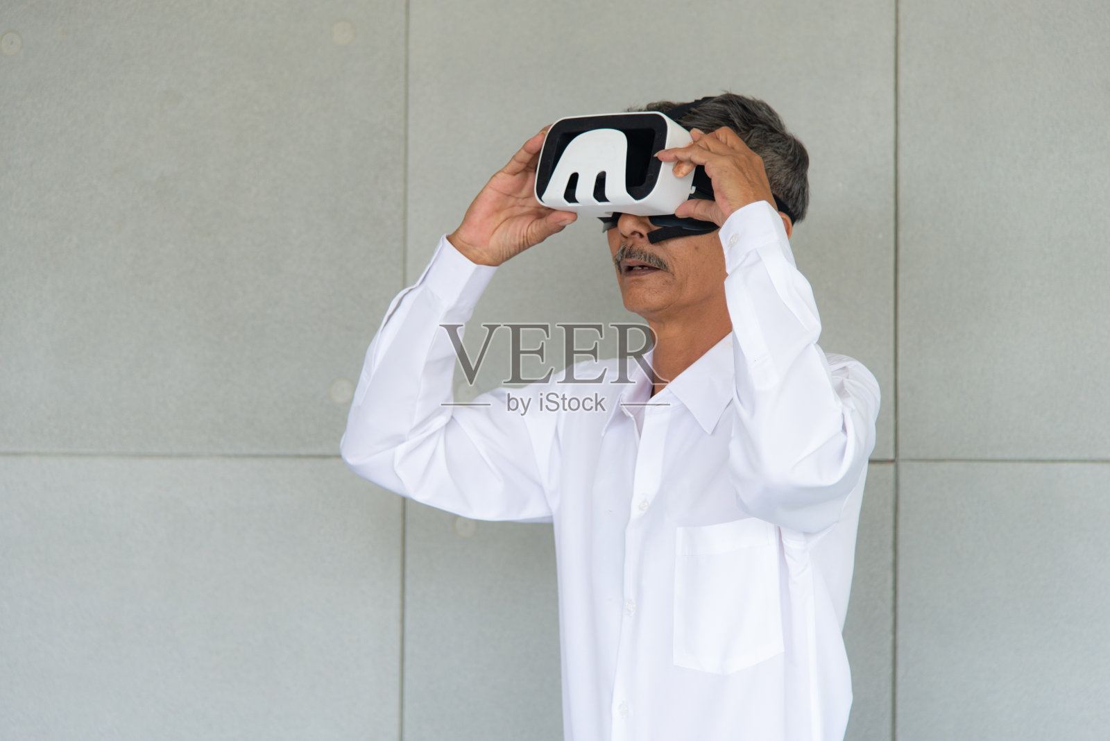 亚洲男子与白衬衫玩游戏，使用虚拟现实设备在客厅照片摄影图片