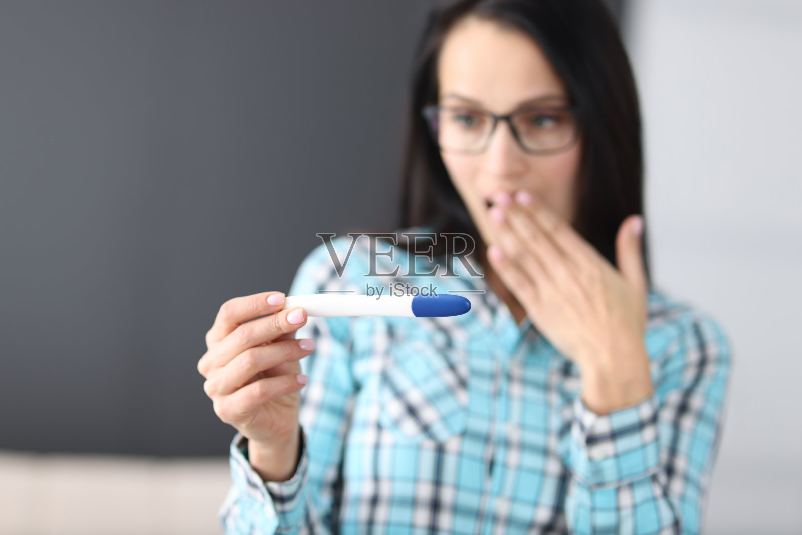 惊讶的年轻女子用手捂着嘴，在家看试卷照片摄影图片