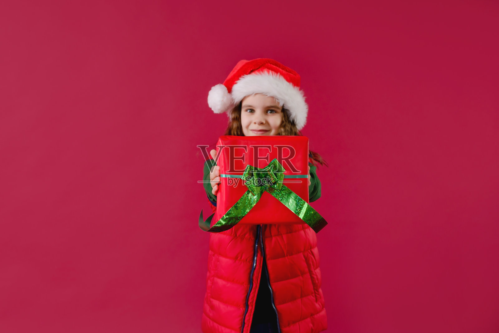一个戴着圣诞帽的女孩手里拿着圣诞礼物。假期,传统概念。照片摄影图片