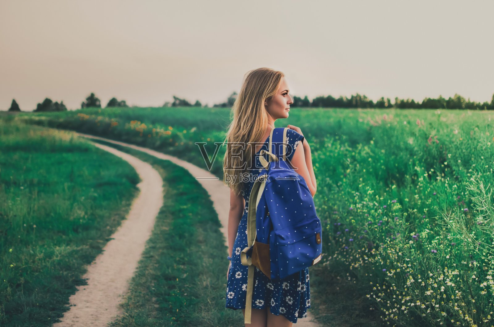 一个穿着裙子背着双肩包的女人站在绿色的田野中间在人行道上照片摄影图片