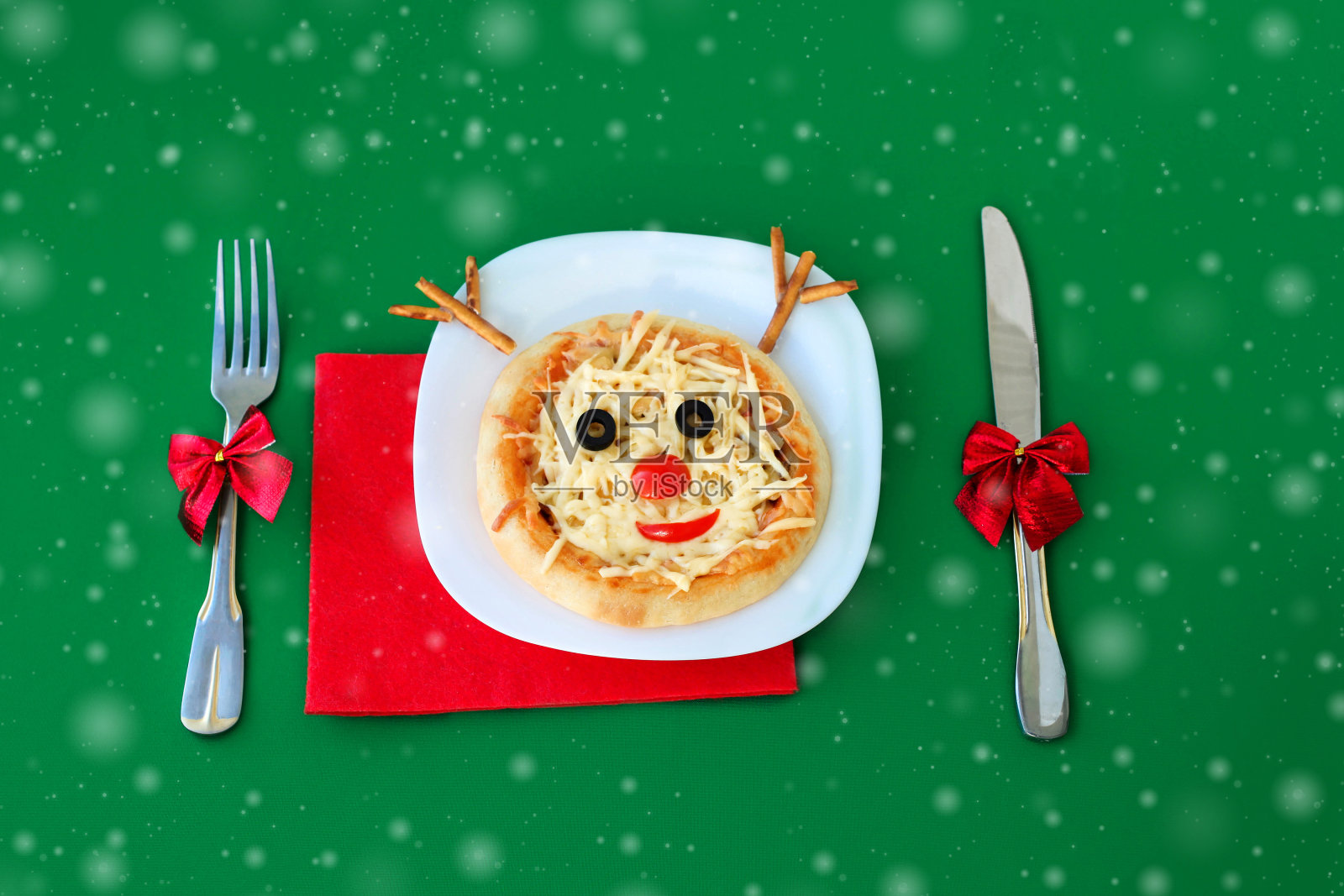 圣诞披萨形状的驯鹿和刀叉在一个绿色的背景。给孩子们的有趣的食物-可爱的鹿。照片摄影图片