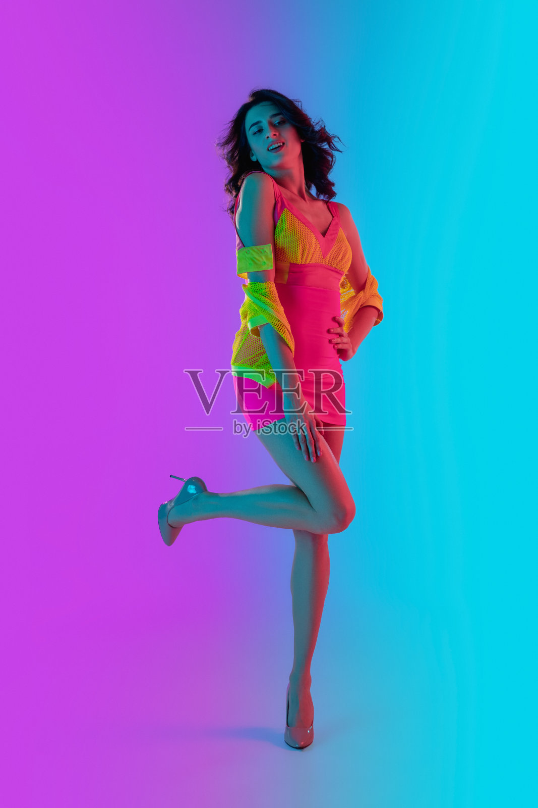 美丽诱人的女孩在时尚的深红色和黄色服装上明亮的梯度粉蓝色背景在霓虹灯照片摄影图片