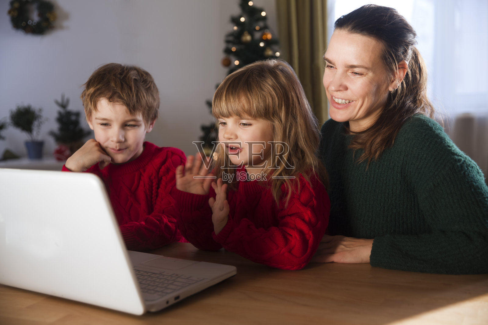 家庭母亲和两个孩子看着笔记本电脑，挥手，视频打电话给朋友或亲戚呆在家里过圣诞节。照片摄影图片