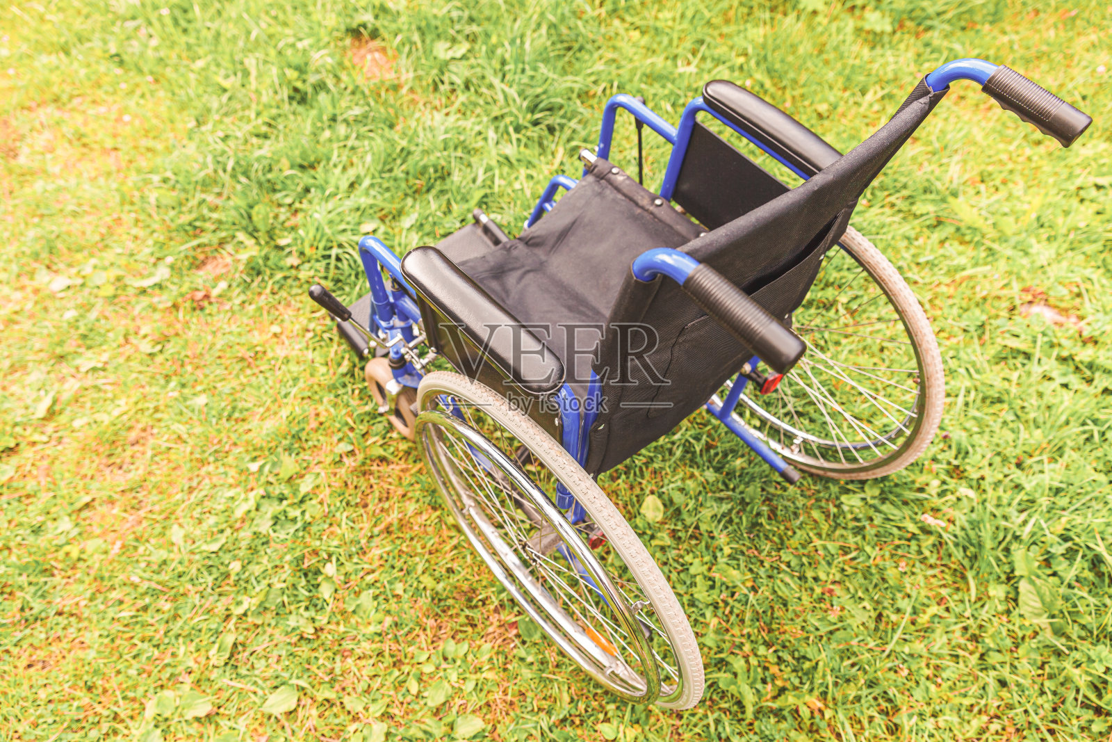 空轮椅站在医院公园的草地上等待病人服务。残疾人专用轮椅停放在户外的自然环境中。障碍的象征。医疗保健理念照片摄影图片