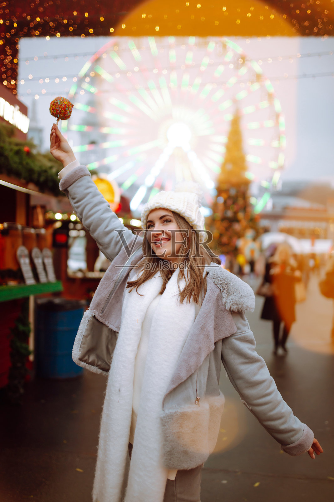 圣诞市场上拿着焦糖苹果的年轻女子。照片摄影图片